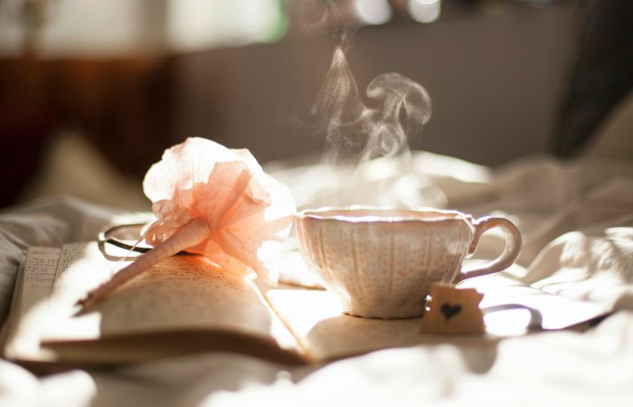 Person journaling in morning light beside a cup of herbal tea